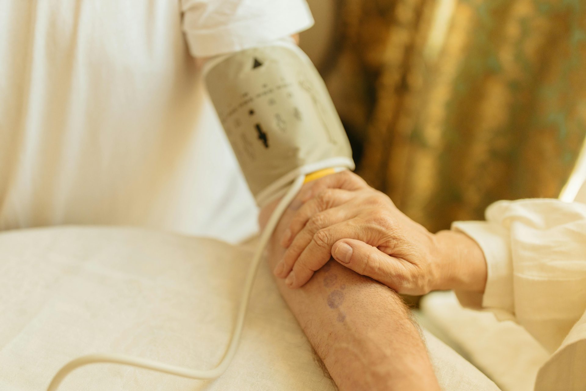 Nahaufnahme einer Blutdruckmessung am Arm eines älteren Erwachsenen in einem Innenraum. Sanftes Licht.